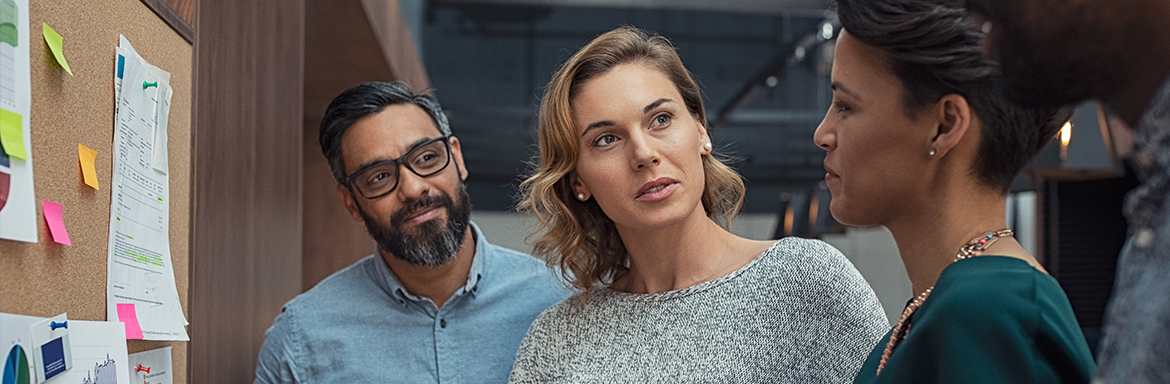 Three people in front of a cork board discussing ideas