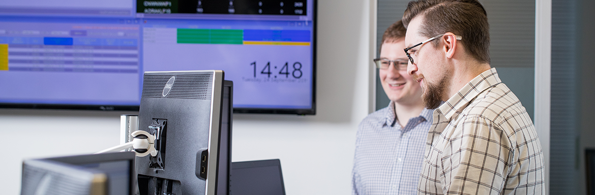 Two people standing in front of a computer in discussion