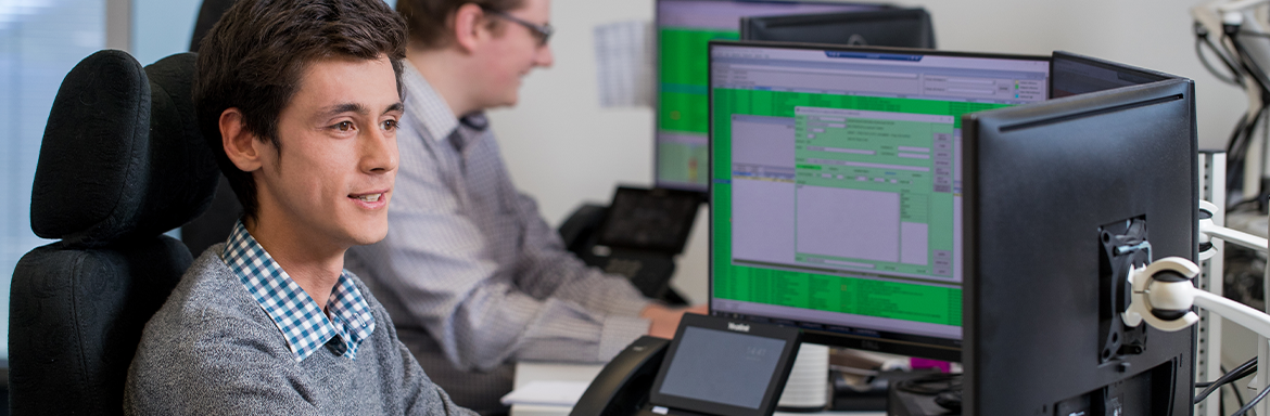 A Jade software developer in front of his computer working on code his colleague in the background