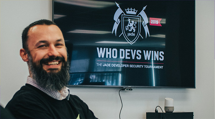 A Jade employee sitting in a meeting room infront of a TV displaying Who Devs Wins, the Jade Developer Security Tournament