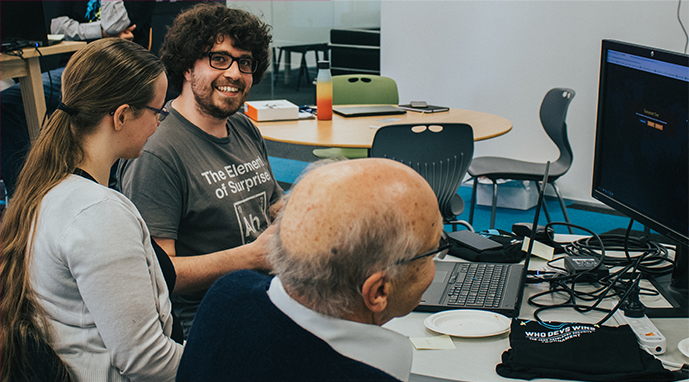 Three Jade employees sitting around a table and computer screen collaborating on development work